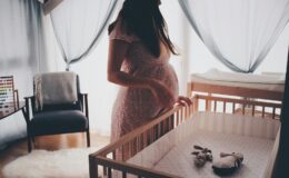 woman in white lace sleeveless dress standing beside brown wooden crib