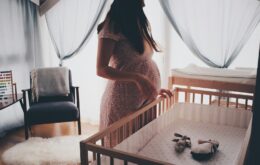 woman in white lace sleeveless dress standing beside brown wooden crib